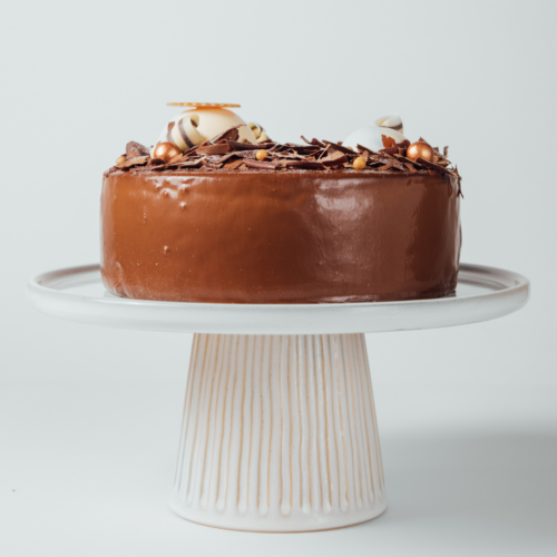 Chocolate cake with decorative toppings on a white cake stand.