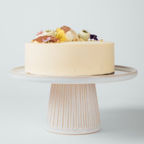 Creamy cake on a decorative stand with floral toppings.