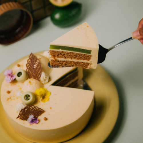 Person serving a slice of decorated cake with flowers and fruit.