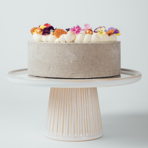 Cake with cream frosting and colorful edible flowers on a stand.