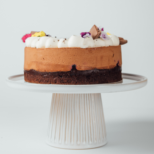 Chocolate mousse cake with whipped cream and edible flowers on a white stand.