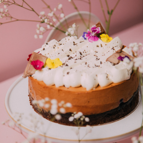 Chocolate cake with whipped cream, flowers, and chocolate pieces on a white plate.