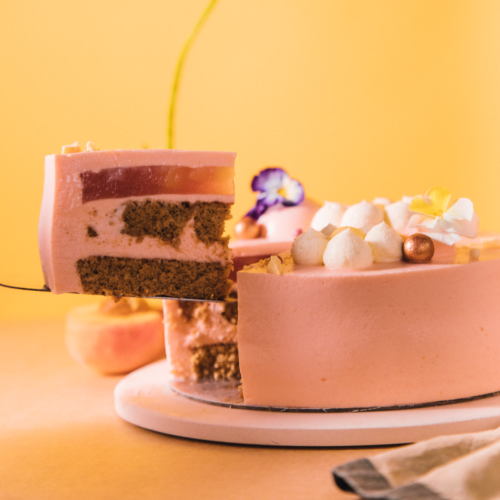 Pink layered cake with a slice being lifted, decorated with flowers and meringues.