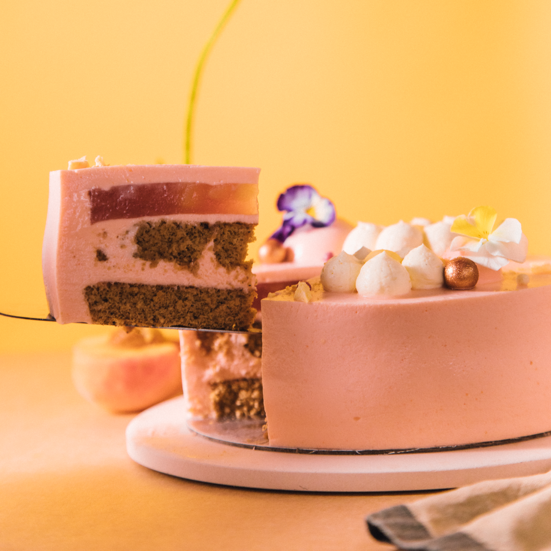 Pink layered cake with a slice being lifted, decorated with flowers and meringues.