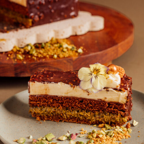 Slice of layered chocolate cake with edible flower garnish on a plate.