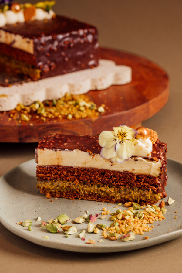 Slice of layered chocolate cake with edible flower garnish on a plate.