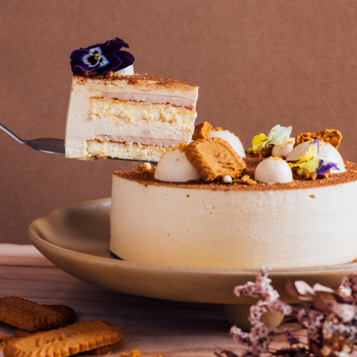 A slice of layered cake with flowers and cookies on top.