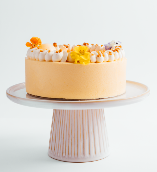 Orange cake with white frosting and flowers on a pedestal stand.