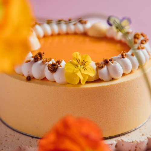 Orange cake with white frosting and yellow flower decoration.