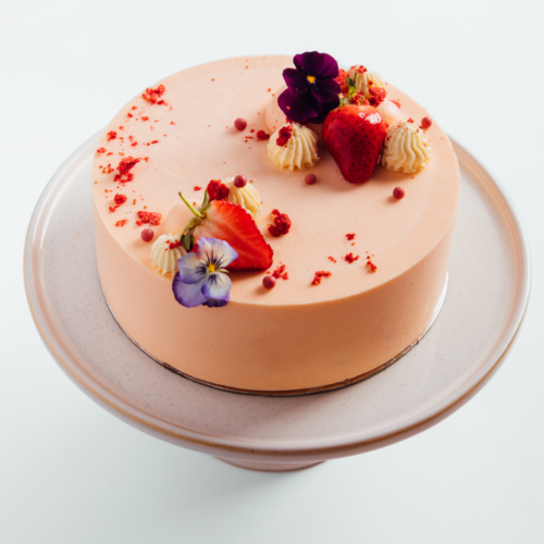 A pink cake with strawberries and flowers on a cake stand.