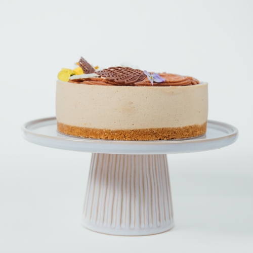 A cheesecake on a white cake stand with chocolate decorations.