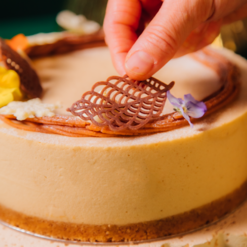 Hand placing chocolate decoration on a cake with flowers.