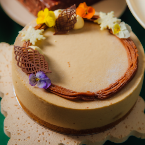 Cheesecake with decorative flowers and chocolate accents on a scalloped platter.