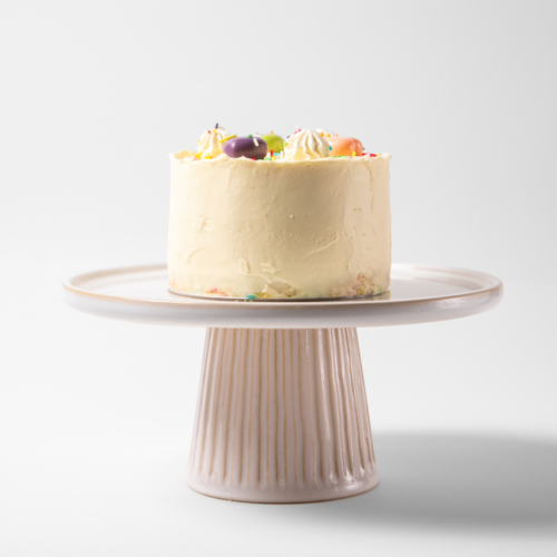 A frosted cake on a white pedestal stand.