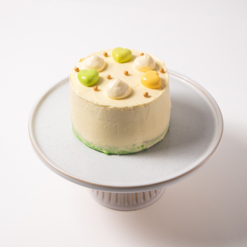 Small frosted cake with colorful decorations on a white stand.