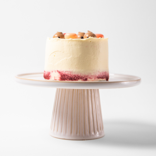 Cake with white frosting and fruit on a pedestal stand.