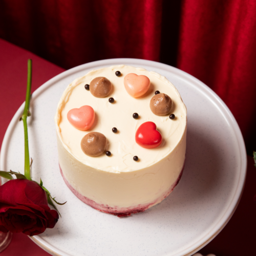 Cake with heart-shaped decorations on a white stand, red rose beside it.