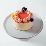 Elegant cake with pink frosting and edible flowers on a stand.