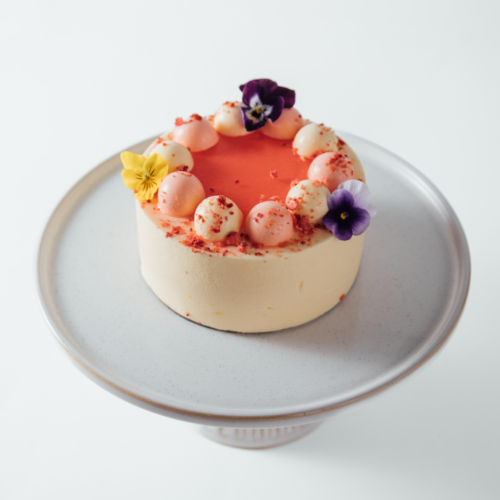 Elegant cake with pink frosting and edible flowers on a stand.