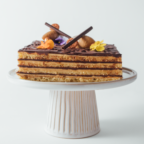 Layered chocolate cake with flowers on a white stand.