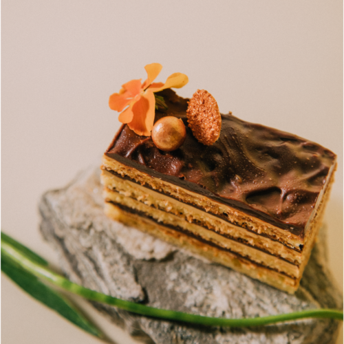 Layered chocolate cake with orange flower garnish on a stone slab.