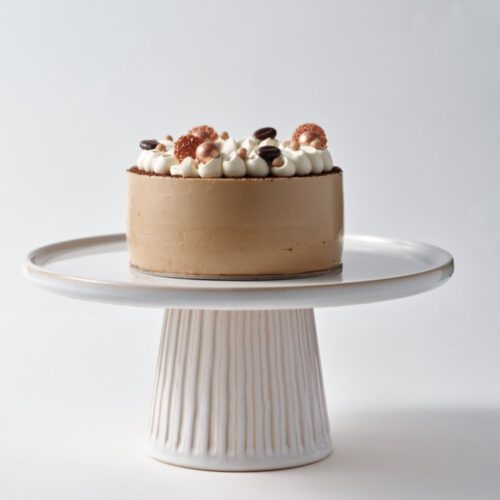 Chocolate cake with cream and decorations on a white cake stand.