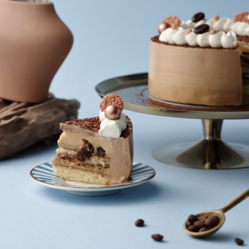 Coffee-flavored cake slice on plate, whole cake in background.
