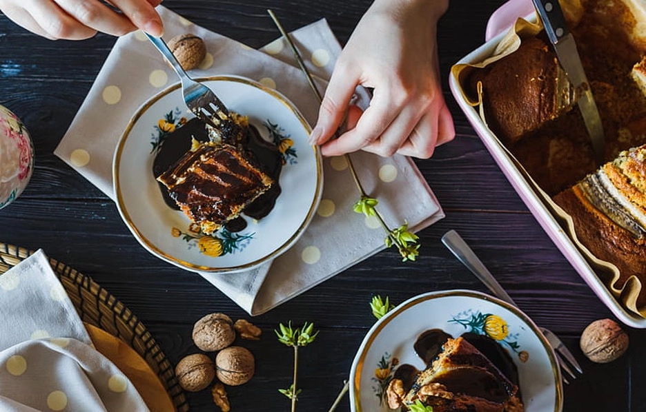 Person eating chocolate cake with walnuts on a table.