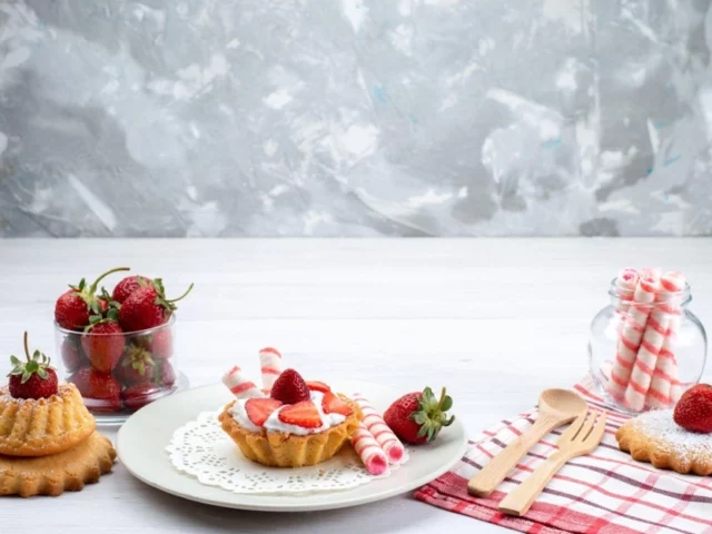 Strawberry shortcake and cookies with wafer rolls on a table.