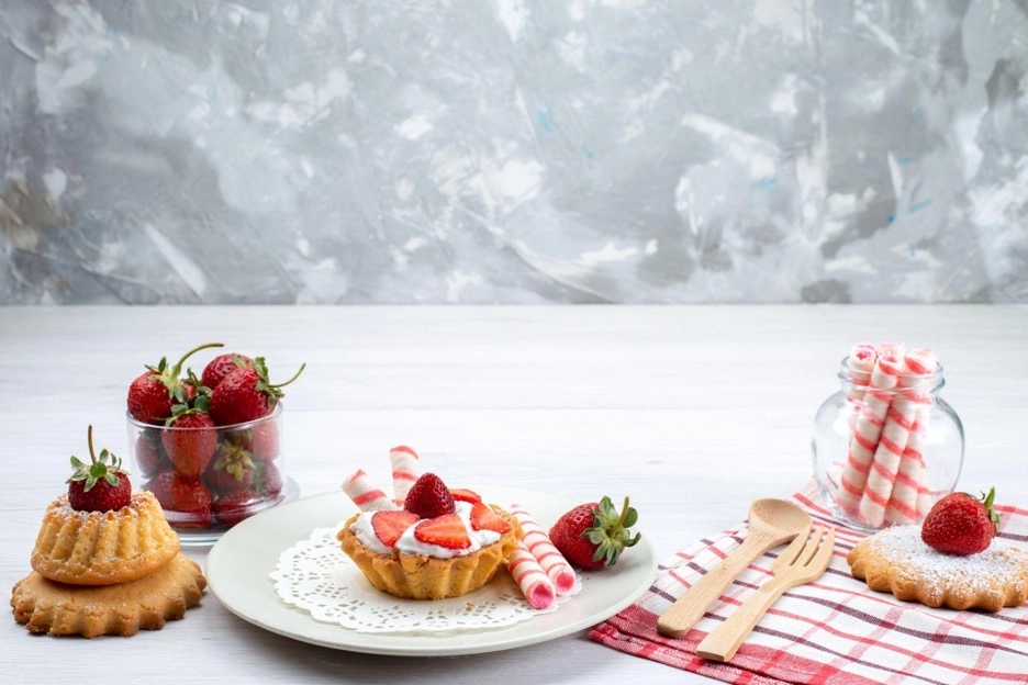 Strawberry shortcake and cookies with wafer rolls on a table.