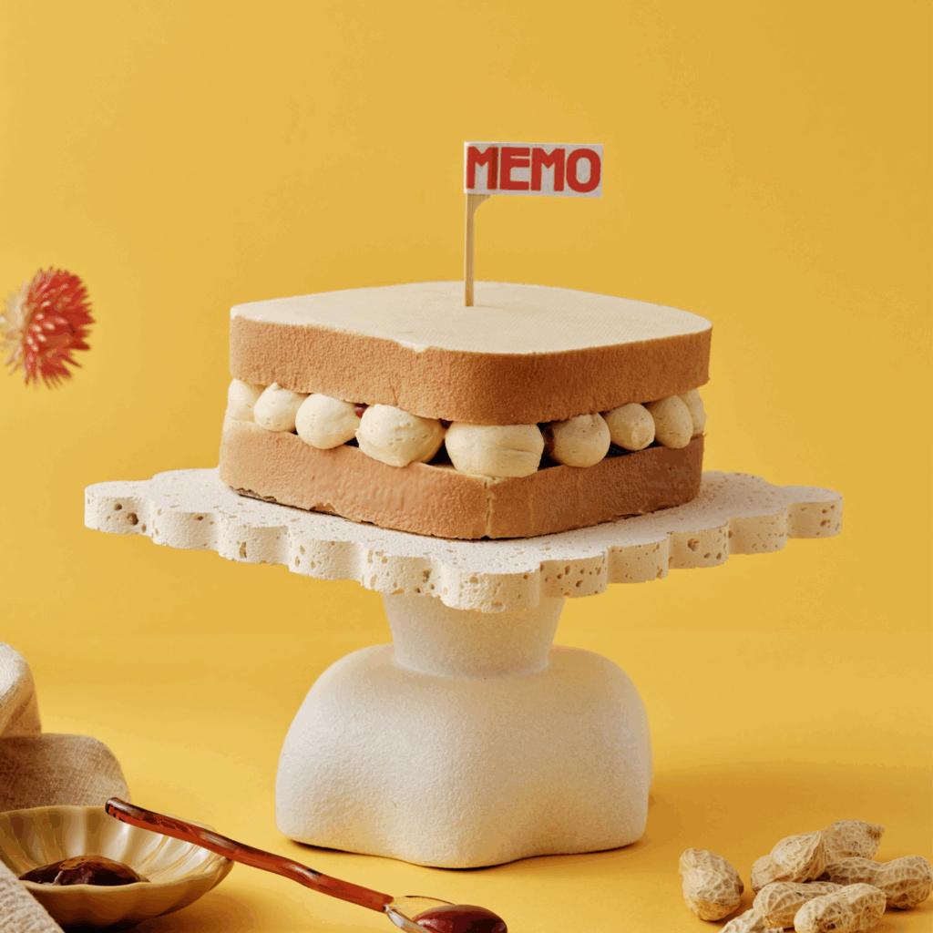 Cake resembling a sandwich on a stand with "MEMO" sign.