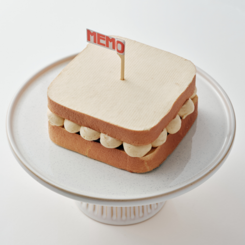 Square cake with cream filling on a stand, topped with a small red flag.