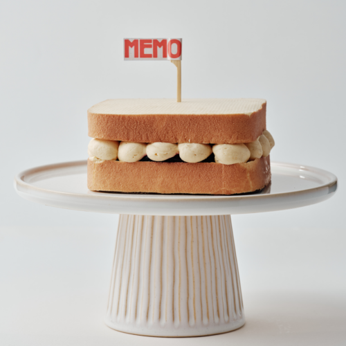 Sandwich with a "MEMO" flag on a white cake stand.