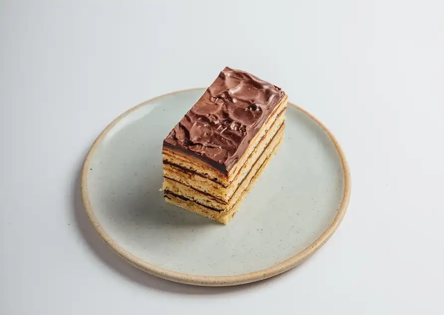 A layered sponge cake with chocolate on top, served on a light-colored plate.