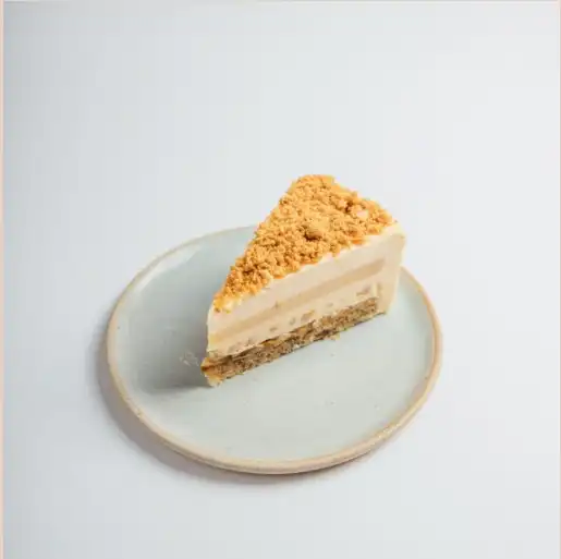 A slice of layered cake with a crumbly topping and light cream filling, served on a simple round ceramic plate
