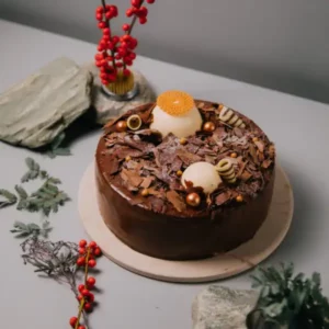 chocolate cake with decorative toppings surrounded by festive greenery and red berries